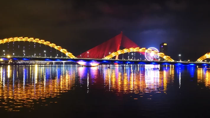 The Dragon Bridge in Da Nang lit in yellow, red and blue at night and reflected in the Han River