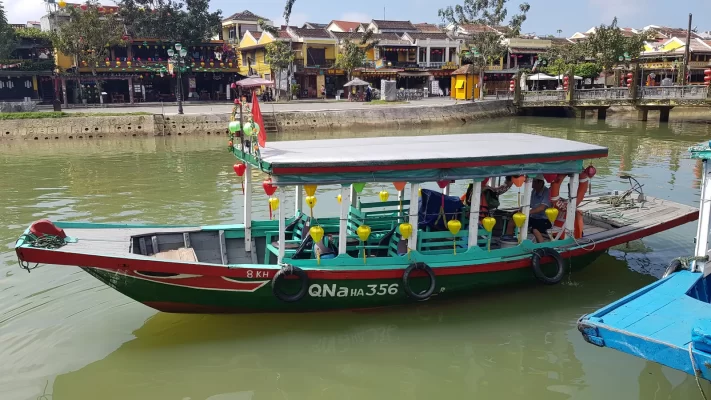 A tourist boat decorated with lanterns on the river at Hoi An, with old shophouses behind