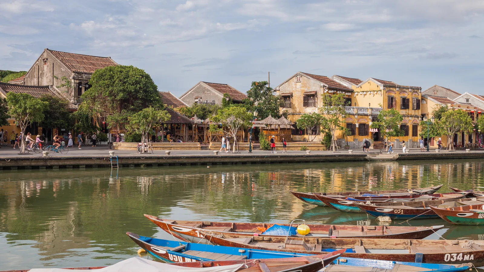Wooden boats moored along the river in front of old yellow buildings in Hoi An