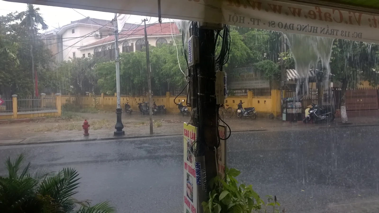Rain falling on Tran Hung Dao street in Hoi An, seen from under an awning