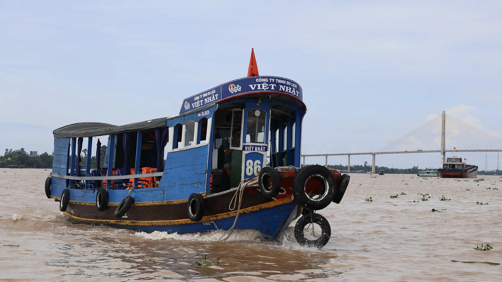 A blue passenger boat on the brown waters of the Mekong River at My Tho