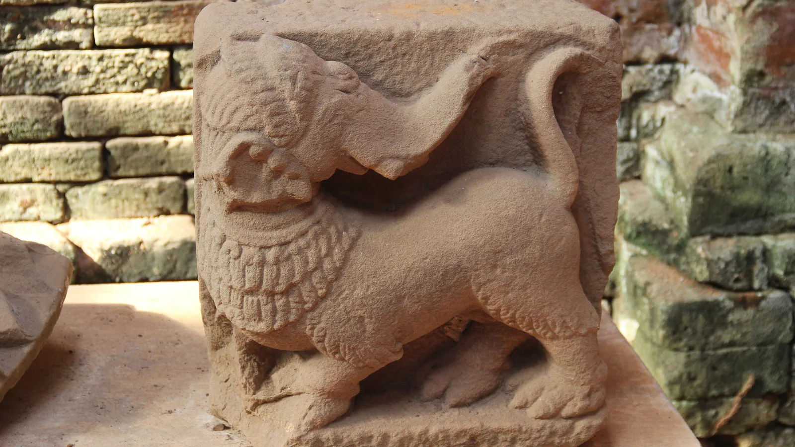 A carved sandstone animal figure beside old brickwork at the My Son Sanctuary